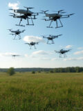 A high-quality image featuring a BVLOS drone flying over a lush green field with trees and a clear blue sky in the background.