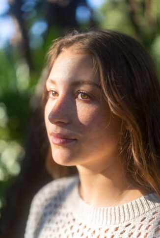 Young woman in warm sunlight with a subtle, guarded expression, reflecting the complex mix of hope and lingering pain in PTSD.