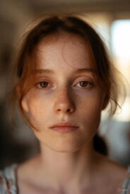 Close-up of a young person with light skin, freckles, and reddish-brown hair, gazing forward with a blank, detached expression typical of abulia.
