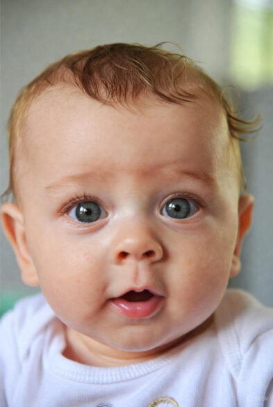 Close-up portrait of a 7-month-old baby with big eyes and open mouth, photographed upside down for a fun effect