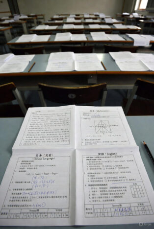 Hundreds of Chinese high school students seated at individual desks in a vast examination hall, heads down writing during the annual Gaokao college entrance exam.