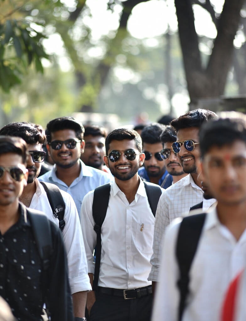 A group of confident young Indian SSC exam aspirants in formal shirts and backpacks walking together outdoors on a sunny day.