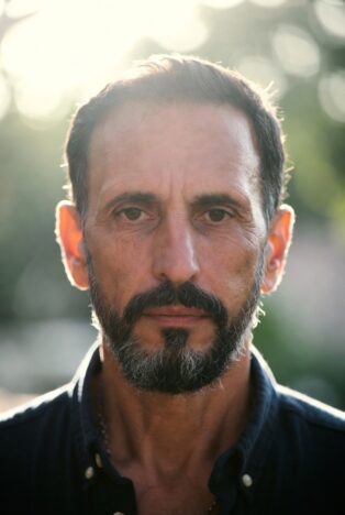 Middle-aged man with beard and worried expression, possible signs of heart condition, dramatic outdoor natural light portrait