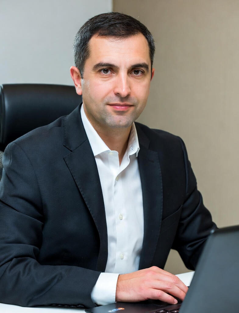 A confident business professional in a dark suit and white shirt sitting at a desk, typing on a laptop, representing focused crisis communication management.