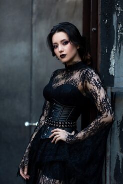 Beautiful Asian woman in elegant black lace gothic dress with corset belt, dark lipstick, posing against distressed industrial door