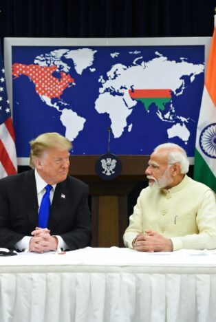 Donald Trump and Narendra Modi sitting face-to-face at a conference table with a world map backdrop and US-India flags, discussing a trade partnership.