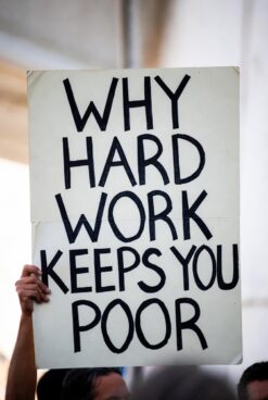 Close-up of handwritten sign saying "WHY HARD WORK KEEPS YOU POOR"