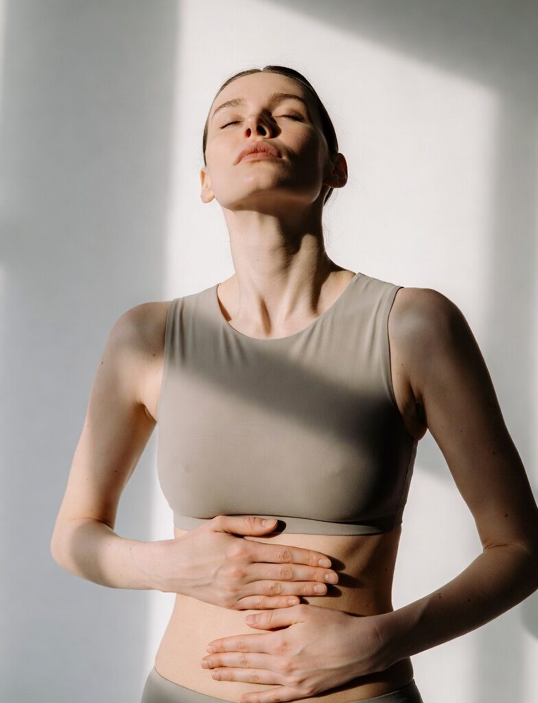 Young woman in beige sportswear gently holding her abdomen, illustrating the gut-skin connection, wellness concept