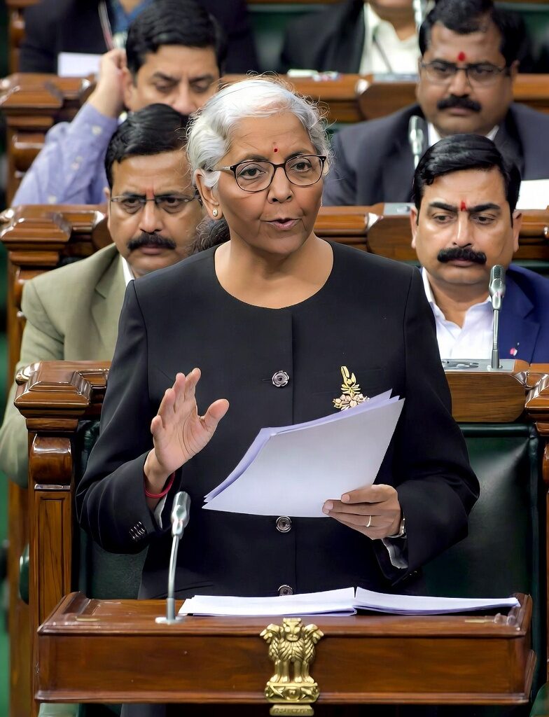 Nirmala Sitharaman addressing Parliament during the Union Budget 2026 presentation, in a black outfit, gesturing with documents, with seated parliamentarians in view.