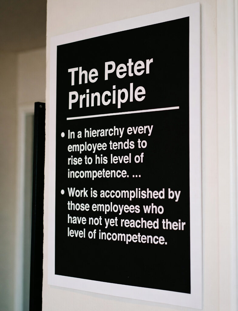 The Peter Principle explained on a black poster: "In a hierarchy every employee tends to rise to his level of incompetence."