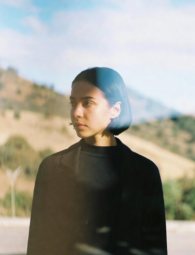 MVH: Escaping the Minimum Viable Human Trap(2026) A thoughtful young woman with a short bob haircut gazing into the distance, symbolizing escape from the Minimum Viable Human (MVH) trap, with a blurred natural landscape in the background.