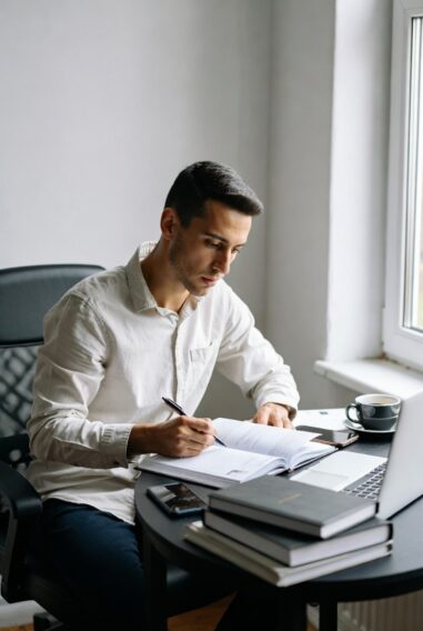 Man studying for PMP exam at desk with books, laptop, and coffee.