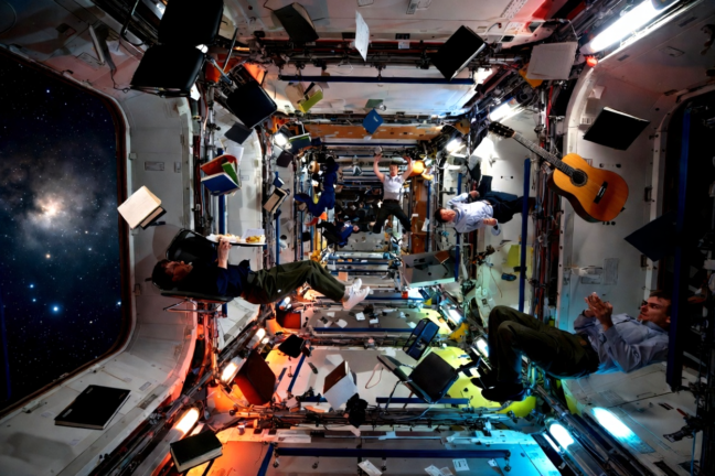 People and objects floating freely in zero gravity inside a space station with a guitar and nebula visible